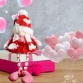 Gestrickte Valentinstag-Gnom-Puppe mit weißen Zöpfen auf einer Geschenkbox-Deko - Weibliche Perlenbeine Puppe