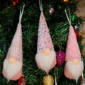 Tre gnomi di Natale rosa con cappelli di maglia appesi a un albero di Natale verde - Stile Rosa Paillettes (D)