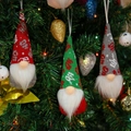 Close-up of knit Christmas gnomes in red, green, and gray hanging on a festive tree branch - HO Pattern Red Green Gray Style (E)