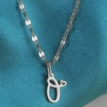 Macro-opname van zilveren letter O-hanger met een klein hartje aan een fijne schakelketting - Staal-O