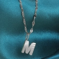 Detail of silver letter M pendant with sunray pleated texture on blue silk background - Letter M / Silver