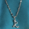 Zilveren ketting met cursieve letter R hanger en hartdetail op blauwe zijden achtergrond - Staal-R