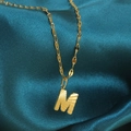 Gouden M-letter hanger ketting met radiale textuur op elegante groenblauwe zijden stof - Goud-M