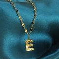 Gouden ketting met letter E hanger en zonnestraaltextuur op donkerblauwe zijden stof - Goud-E
