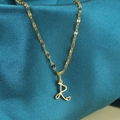 Gouden ketting met cursieve letter R en hartje op elegante pauwblauwe satijnen stof - Goud-R