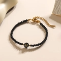 Detail van zwarte gefacetteerde kralenarmband met gouden letter B bedel en sluiting - Letter - B