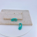 Close-up of two turquoise macaron-style lobster clasps on a textured stone background - Turquoise Green