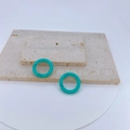 Detailed view of turquoise lacquered copper spring rings on a beige travertine surface - Cyan Blue