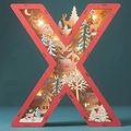 Detail of wooden letter X lamp showing layered Christmas scene with deer and cabin - Letter X