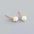Macro detail of white round pearl earrings with golden four-claw setting on gray background - Gold