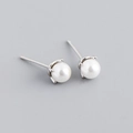 Macro shot of minimalist white pearl stud earrings with silver four-prong setting details - White Gold