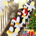 Tres pingüinos de Navidad de peluche con gorros de invierno en una escalera decorativa - Juego de Pingüinos Con Luces Y Manta de Nieve