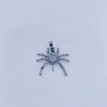 Vista macro de colgante de araña con circonitas blancas y gema verde sobre metal plateado - Colgante Estilo Araña / Colgante Negro de Pistola (Sin Cadena de Perla)