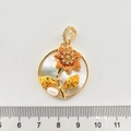 Dettaglio del ciondolo a fiore con smalto arancione e perla naturale accanto a un righello - Margherita dorata