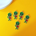 Five green enamel alien charms with red hearts and golden hooks on yellow background - Alien with Heart