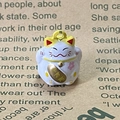 Macro shot of purple Maneki Neko charm with pink cherry blossom and gold coin detail - Yellow