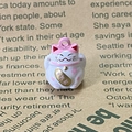 Macro view of lucky cat charm with cherry blossom details and golden plaque - Pink