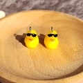 Nahaufnahme von Harz-Entenanhängern mit Sonnenbrille und Metallringen auf Holztablett - Ente mit Sonnenbrille