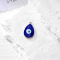 Dettaglio del ciondolo malocchio con smalto blu e finitura dorata su sfondo pietra - Design a Goccia Dorata / Oro