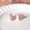 Macro shot of two pink flocked squirrel charms with metal rings on a white porcelain plate - Squirrel Eating Apple