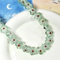 Détail de perles de fleurs en verre vert translucide avec centres rouges sur plateau - Fleur Vert Clair