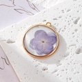 Vue macro d'un pendentif fleur séchée violette en résine avec cadre rond doré - Floral Violet Clair