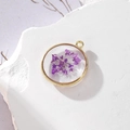Dettaglio macro di un ciondolo dorato rotondo con fiore secco viola e glitter per gioielli - 5 GH55