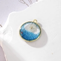 Dettaglio macro del ciondolo tondo dorato con margherita essiccata bianca e glitter blu - 6 GH55