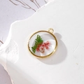 Vista macro di un ciondolo tondo dorato con fiori secchi e foglie di felce incorporate - 7 GH57