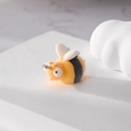 Macro shot of a yellow flocked bee charm with metal ring on a white stone pedestal - Bee
