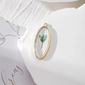 Detail of oval golden pendant featuring a real light blue dried flower in resin - Light Blue Flower Style (GH26)