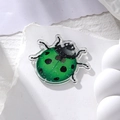 Macro detail of a green glitter acrylic ladybug pendant on a white stone background - Green Ladybug