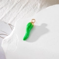 Macro view of a green chili pepper alloy pendant with gold ring on white stone - Green