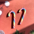 Close-up of rainbow striped candy cane pendants with metal rings on festive red background - Thin Rainbow Candy Cane