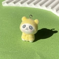 Makro-Detail eines gelb beflockten Panda-Anhängers mit Metallring auf grünem Grund - Gelber Regenmantel Panda
