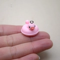 Detail shot of a miniature pink resin duck pendant showing small scale on a finger tip - W20 / Pink Duck