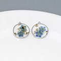Détail de pendentif rond en résine avec fleurs séchées bleues et feuilles d'or en argent - Myosotis Bordé d'Argent