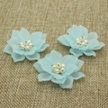Tre toppe a forma di fiore di camelia in resina azzurra con perle su sfondo di lino rustico - Petalo Appuntito con Perla Blu
