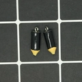 Macro view of two black pencil charms with silver metal rings on a measuring mat - Black Crayon
