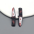 Macro shot of two bloody dagger charms for Halloween jewelry DIY crafts with red splatter - Serrated Dagger