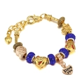 Detailed close-up of golden charm bracelet with blue beads, heart charms and Paris suitcase - 16cm / Blue
