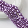 Perlas de vidrio morado lavanda de varios tamaños en una bandeja de cerámica blanca - Púrpura