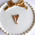 Detalle macro de colgante de lazo crema con tres diamantes pequeños para joyería DIY - Marrón