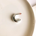 Close-up of a minimalist C-shaped silver hoop earring on a white ceramic plate - Silver Small Crescent