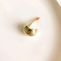 Close-up of golden C-shaped hoop earring with textured waves on a ceramic tray - Gold Leaves