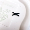 Dettaglio di un accessorio per capelli nero lucido a forma di X con cuore su un vassoio - Forma X a Cuore (kp6107) / Fiocco Cuore Nero