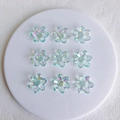 Macro shot of 9 aurora acrylic flower pendants on a white tray for DIY jewelry making - 21x6mm