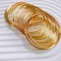 Detailed close-up of polished gold stackable wire bracelets on a white textured tray - One Roll / Gold