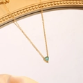 Detail einer goldenen Edelstahl-Herzkette mit blaugrünem Edelstein auf Satinstoff - März (Hellblau)