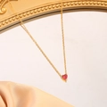 Close-up of a red heart birthstone necklace with a gold chain on satin fabric - July (Rose Red)